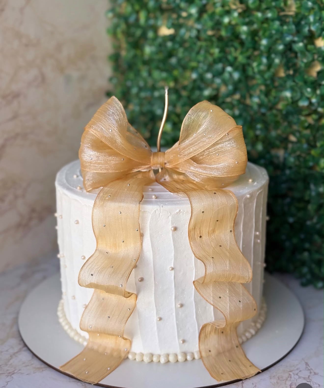 Bolo branco com pérolas e um grande laço de organza dourado